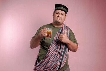 A man in a plaid shirt and a turban holding a glass of tea. He is smiling and giving a thumbs up