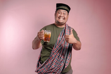 A man in a plaid shirt and a turban holding a glass of tea. He is smiling and giving a thumbs up