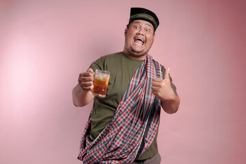 A man in a plaid shirt and a turban holding a glass of tea. He is smiling and giving a thumbs up