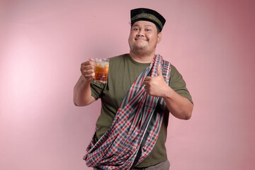 A man in a plaid shirt and a turban holding a glass of tea. He is smiling and giving a thumbs up