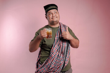 A man in a plaid shirt and a turban holding a glass of tea. He is smiling and giving a thumbs up