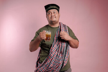 A man in a plaid shirt and a turban holding a glass of tea. He is smiling and giving a thumbs up