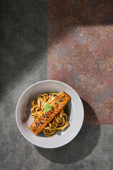 Salmon steak with udon noodles, bright dramatic lighting, overhead ceramic bowl composition