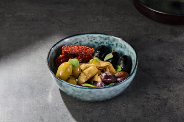 Antipasti bowl with olives, sun-dried tomatoes, and artichoke, moody lighting, overhead composition