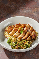 Ptitim with sliced chicken fillet under bright directional lighting, closeup on artisanal ceramic plate