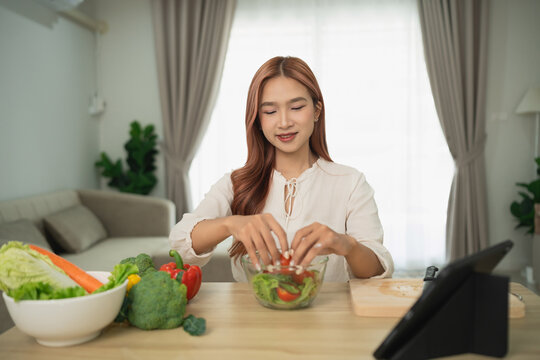 Young woman preparing fresh salad in modern kitchen, enjoying healthy lifestyle, surrounded by vibrant vegetables and cooking tools
