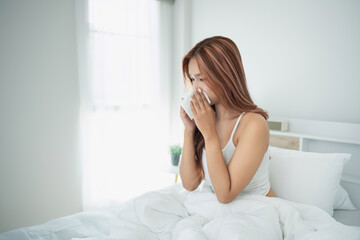 Young woman sitting on bed with cup in hands, morning light streaming through window, cozy atmosphere, lifestyle concept, deep in thought or reflection