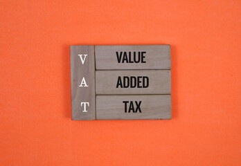 Wooden Block with the words VAT 'value, added, tax' on an Orange Background