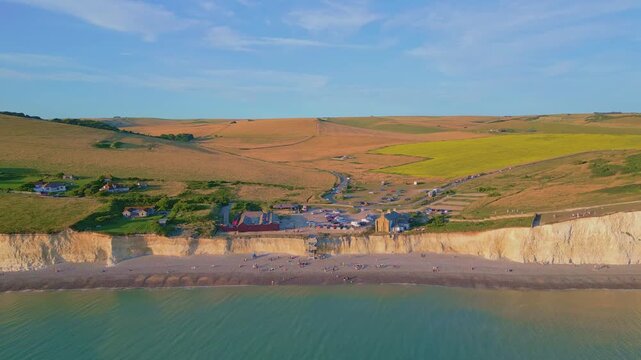 Sunrise aerial dolly-in shot of Birling Gap and the Seven Sisters cliffs, with golden light reflecting on the calm sea.