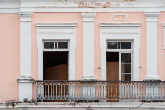Historic facade of a pink building with white columns and a balcony, dated 1868