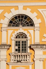 Obraz na płótnie Canvas Ornate arched window with a decorative balcony on a yellow building facade in sunlight