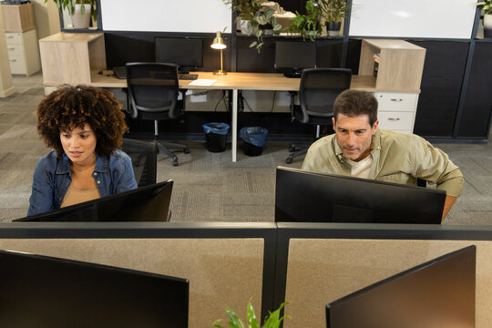 Working diverse coworkers typing at adjacent desks in open-plan office, with computer monitors