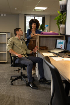 Diverse office colleagues reviewing data charts in open-plan cubicle, with laptop and yoga mat
