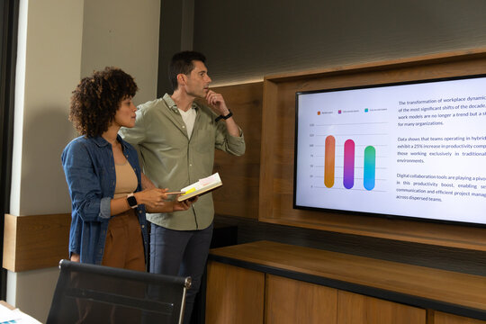 Diverse colleagues studying hybrid work charts on display in office with notebook, copy space