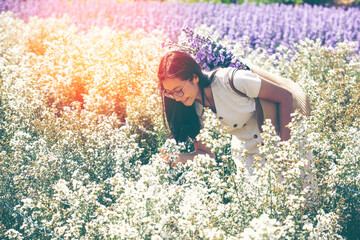 Photo of asian young woman in white dress holding bag full of bouquet of flowers, while walking...