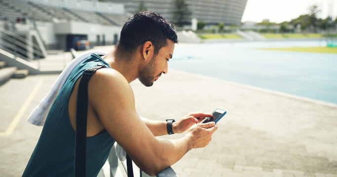 Athlete, man and browsing with phone at stadium for social media, fitness app and event agenda. Male person, rest and mobile for texting contact, sports progress results and information on tournament - Powered by Adobe