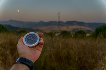 Hand holding compass navigating in mountain landscape at dusk with moon