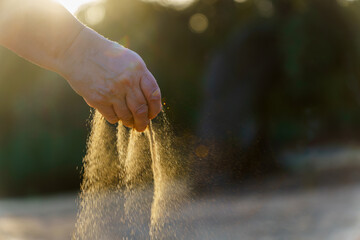 Hand dropping sand with sun shining in the background, symbolizing the passage of time