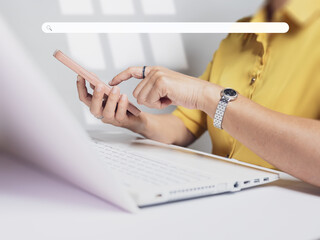 Person using smartphone while working on laptop in modern workspace during daytime