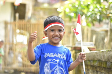 A 3-year-old child with a red and white ribbon on his head and a red and white flag in his hand....