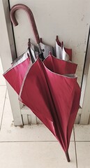 A bright red umbrella, folded and leaning against a wall, signifies the end of the rainy season or...