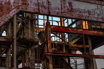 Ein Blick in das rostige Herz einer verlassenen Industrieanlage, wo die Zeit ihre Spuren in Form von Rost und Verfall hinterlassen hat. Die warmen Farben des Sonnenuntergangs oder Sonnenaufgangs spieg