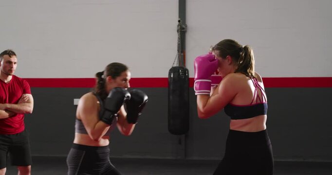 At coach's signal two female trainees sparring wearing gloves on mat in boxing gym honing skills