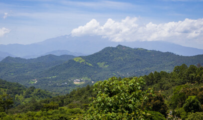 Rolling Hills Under a Summer Sky: A sprawling landscape of layered, green hills unfolds under a...