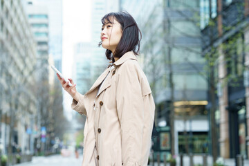スマートフォンを手にビジネス街を歩く女性