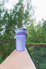 Purple shaker bottle on balcony railing against forest background