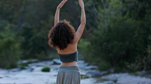 A serene moment captured in nature as a woman with curly hair stands near a tranquil stream, embracing the beauty of the outdoors and the peaceful atmosphere around her.