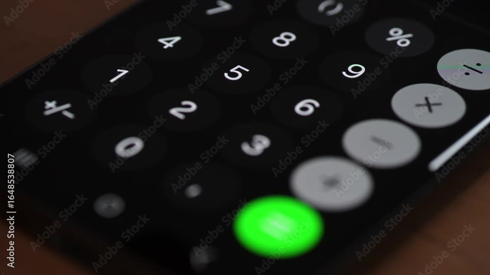 Poster video of a finger pressing a button on a smartphone calculator app. the bright numeric keys and gree