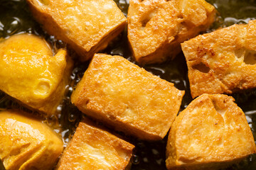 Yellow tofu frying in boiling oil. Top view