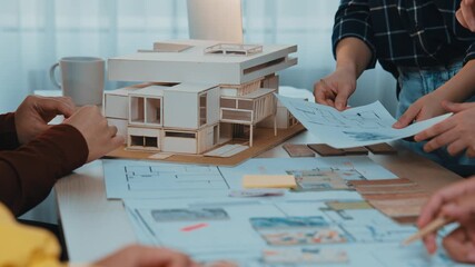 A collaborative team engages in a meaningful discussion about an architectural model and blueprints in a modern office, showcasing creativity and teamwork in design. SACTR