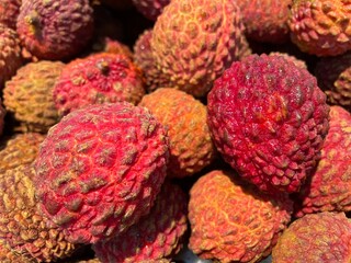 Close-up of fresh red lychees tightly piled, showing bumpy textured skin and natural shine,...