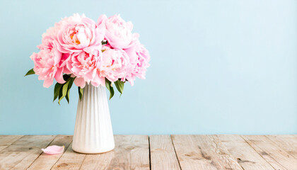 Fototapeta premium Beautiful bouquet of fresh pink peonies in a white vase on a rustic wooden table against a serene light blue background, perfect for home decor and spring aesthetics.