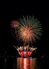 Vibrant fireworks explode over a calm water body, reflecting colorful lights in the night sky.