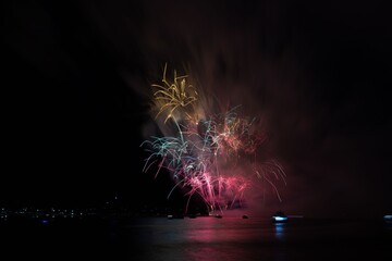Vibrant fireworks explode over a calm water body, reflecting colorful lights in the night sky.