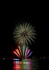 Vibrant fireworks explode over a calm water body, reflecting colorful lights in the night sky.