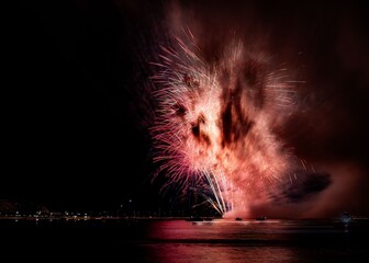Vibrant fireworks explode over a calm water body, reflecting colorful lights in the night sky.