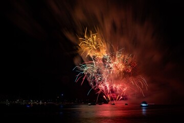Vibrant fireworks explode over a calm water body, reflecting colorful lights in the night sky.