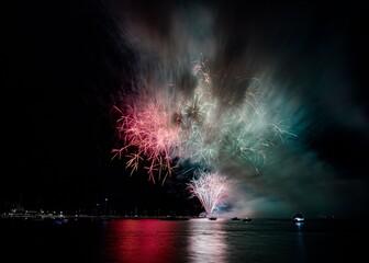 Vibrant fireworks explode over a calm water body, reflecting colorful lights in the night sky.