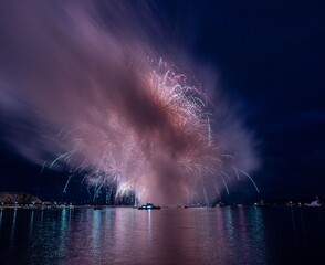 Vibrant fireworks explode over a calm water body, reflecting colorful lights in the night sky.