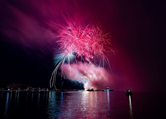 Vibrant fireworks explode over a calm water body, reflecting colorful lights in the night sky.