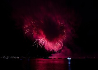 Vibrant fireworks explode over a calm water body, reflecting colorful lights in the night sky.