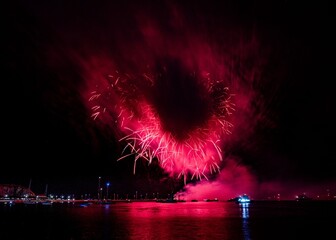 Vibrant fireworks explode over a calm water body, reflecting colorful lights in the night sky.
