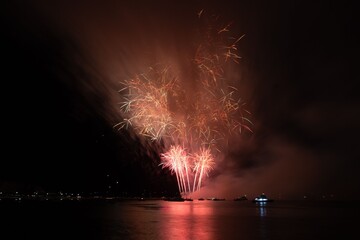 Vibrant fireworks explode over a calm water body, reflecting colorful lights in the night sky.