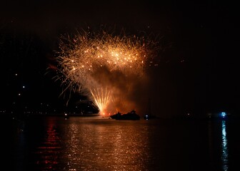 Vibrant fireworks explode over a calm water body, reflecting colorful lights in the night sky.
