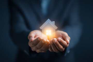 A person holding a glowing house icon with light shining from its window.