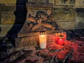 Cross with Christ and skull ornament lit by candle in front of medieval Gothic church, mystical...